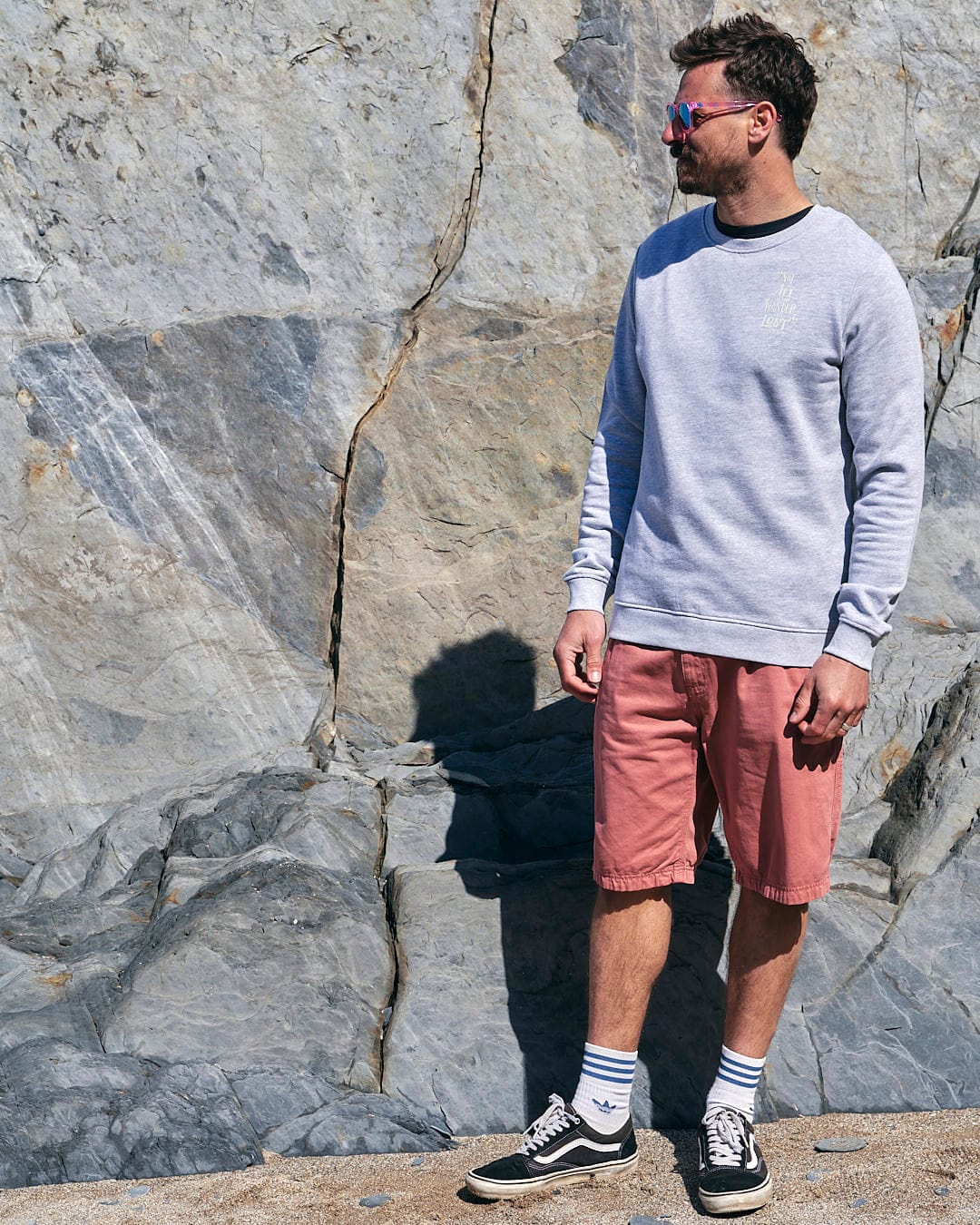 A man wearing Lost Ships - Mens Crew Sweat - Grey from Saltrock standing next to a rock.