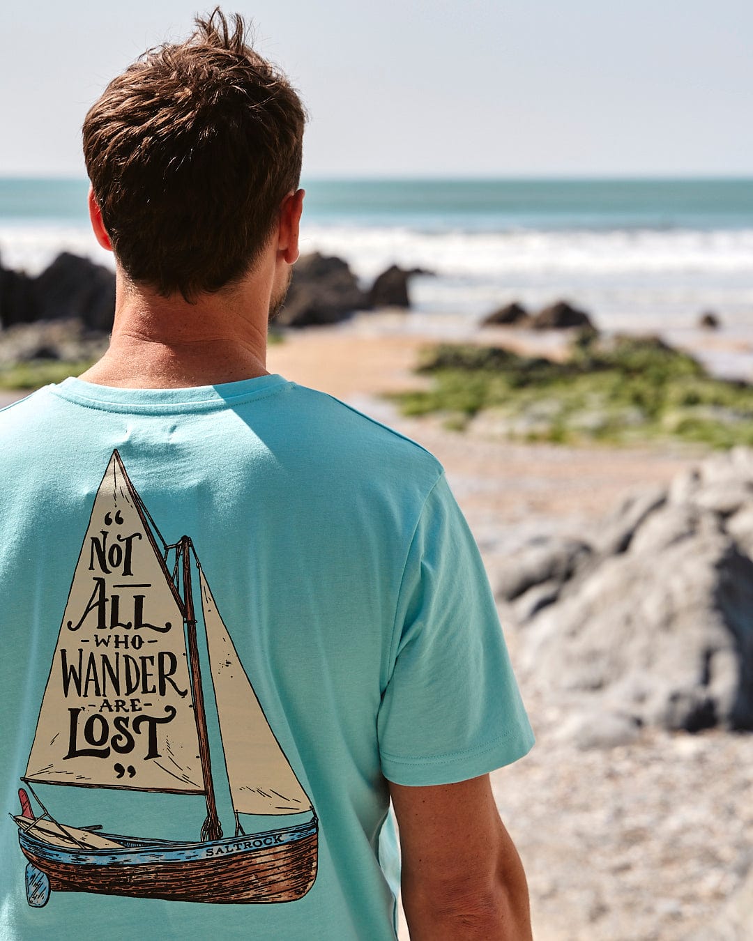 The back of a man wearing a Saltrock Lost Ships - Mens Short Sleeve T-Shirt - Light Blue with a sailboat on it.