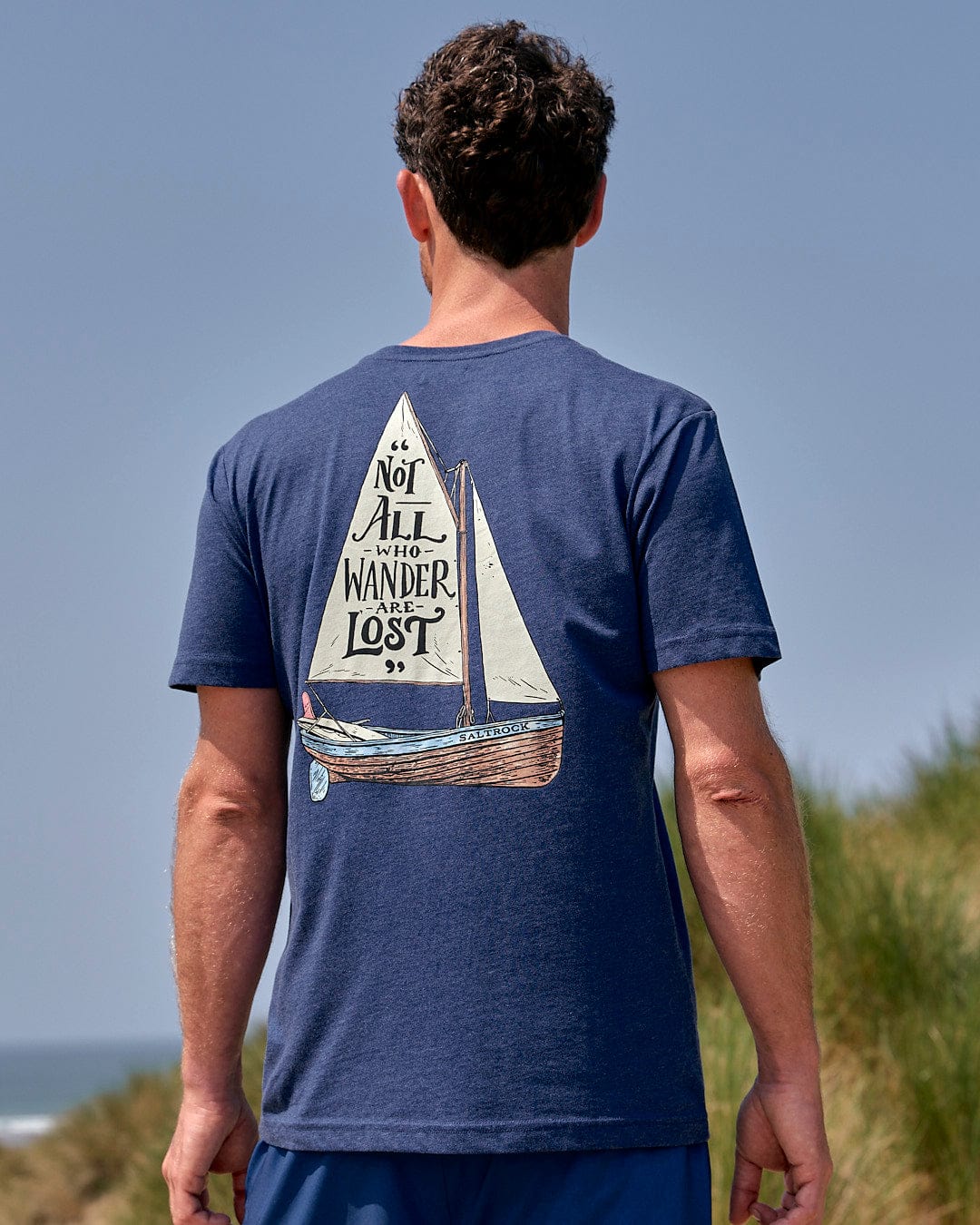 A man wearing a Saltrock Lost Ships - Mens Short Sleeve T-Shirt - Blue with a sailboat on it.