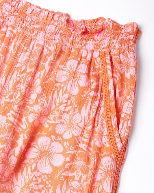 Close-up of a Lottie Hibiscus - Kids Trousers - Orange/Pink fabric with elastic waistband by Saltrock.