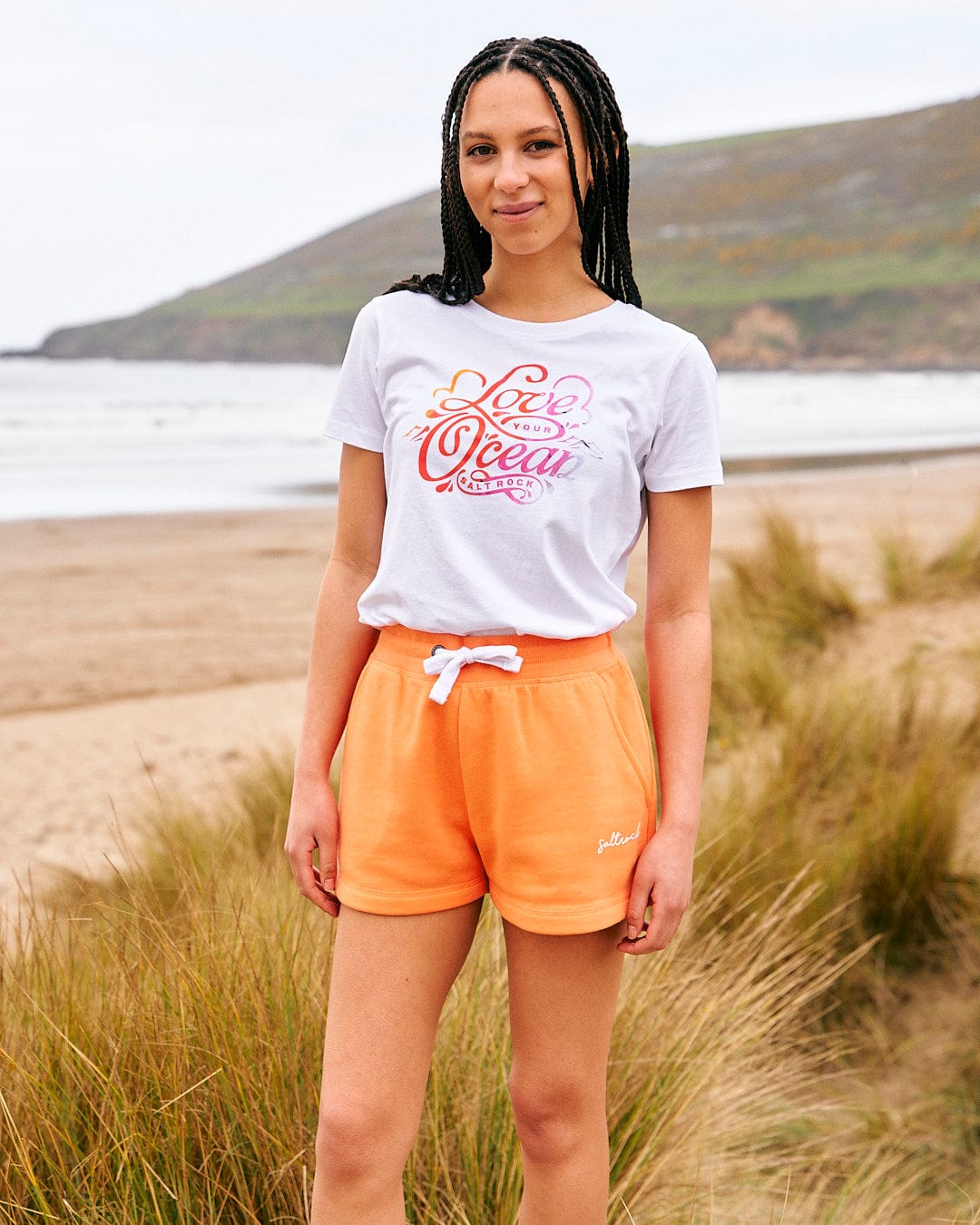 A woman wearing orange shorts and a Saltrock Love Your Ocean - Womens Short Sleeve T-Shirt - White.