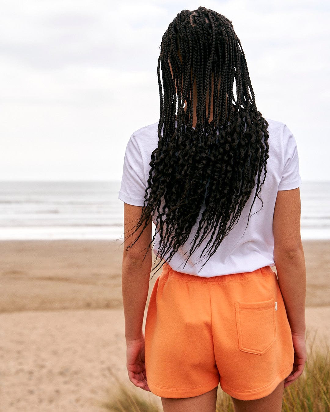 A woman wearing orange shorts and a Saltrock Love Your Ocean - Womens Short Sleeve T-Shirt - White on the beach.