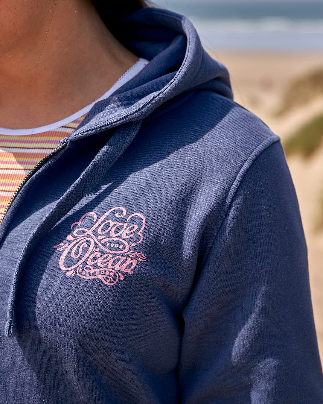 A woman wearing a Saltrock hoodie with the brand name Love Your Ocean - Womens Zip Hood - Dark Blue on it.