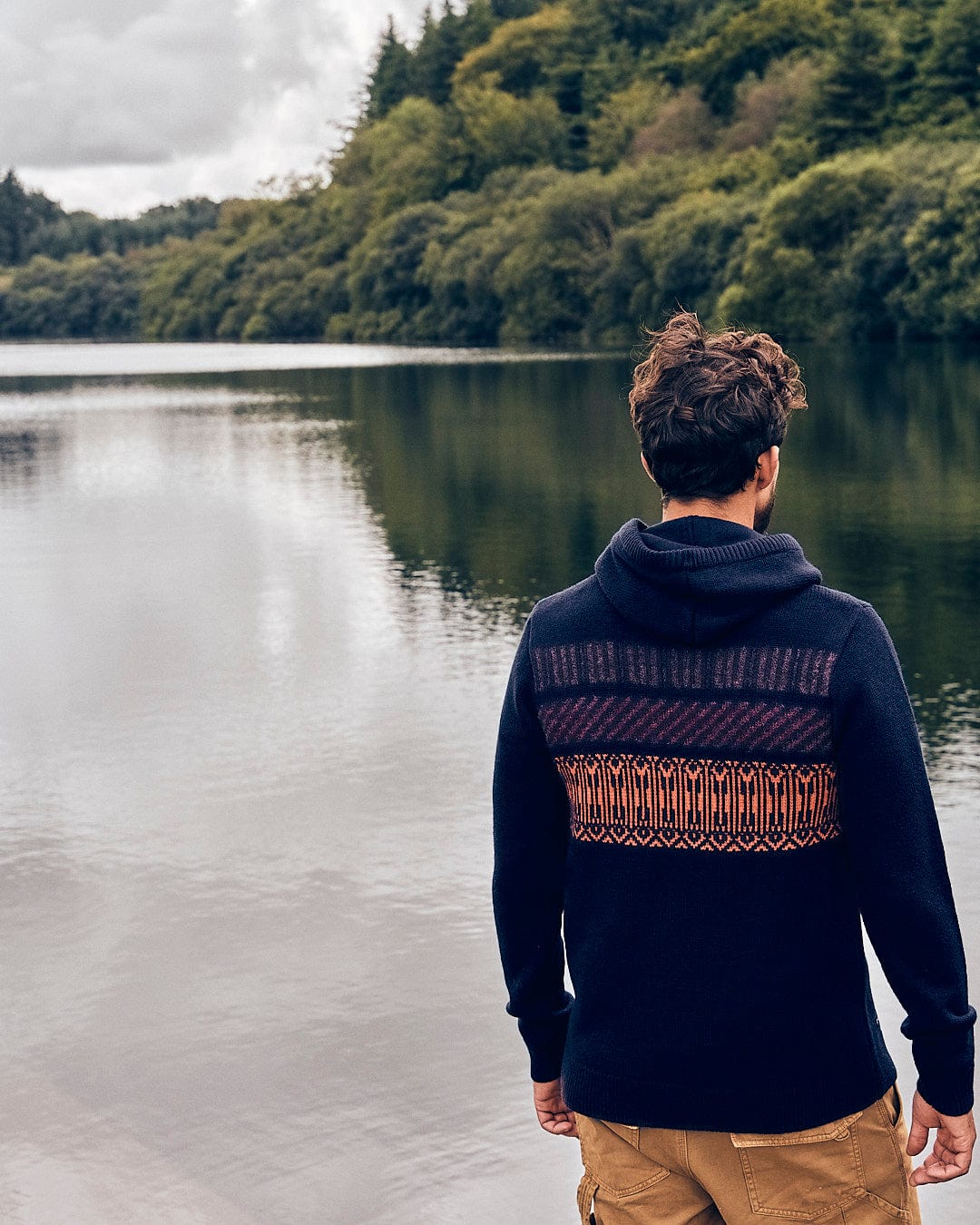 A man standing by a lake wearing a Saltrock Lukas - Mens Knitted Hoodie - Dark Blue.