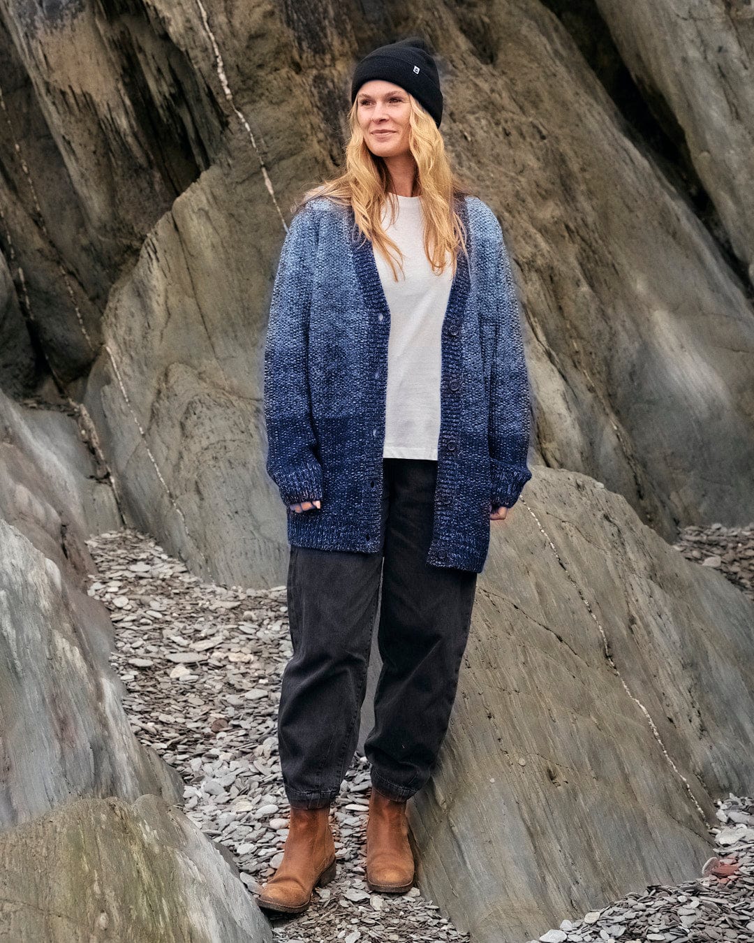 A woman standing on rocks wearing a Saltrock Lynton - Women's Button Cardigan - Dark Blue.