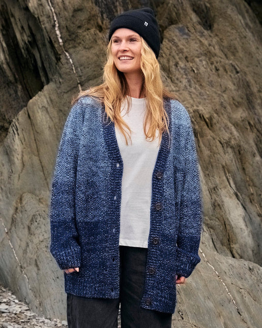A woman wearing a Saltrock Lynton - Womens Button Cardigan - Dark Blue standing in front of rocks.