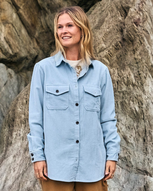 A woman wearing a Maddox - Womens Cord Shirt - Light Blue by Saltrock in front of rocks.