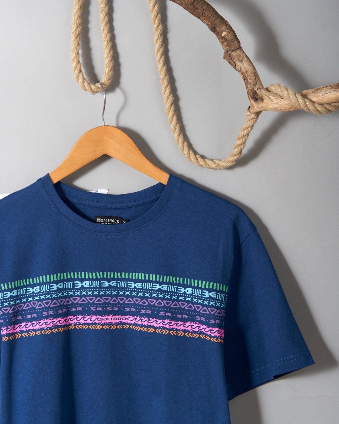A Marks Chest - Mens Short Sleeve T-Shirt in blue cotton with colorful stripes hanging on a rope, featuring Saltrock branding.