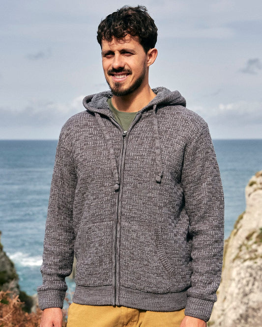 A man wearing the Markus - Mens Borg Lined Knit Hoodie - Grey, showcasing Saltrock branding, stood next to the ocean.