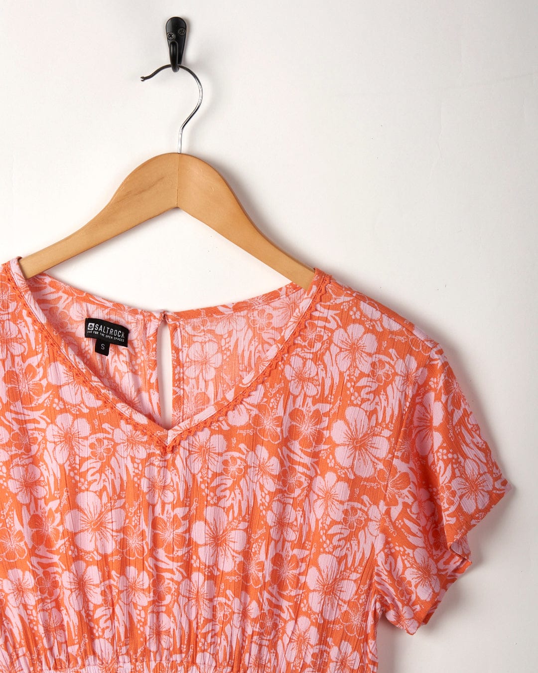 Marla Hibiscus womens dress in pink/orange hanging on a wooden hanger against a white wall.