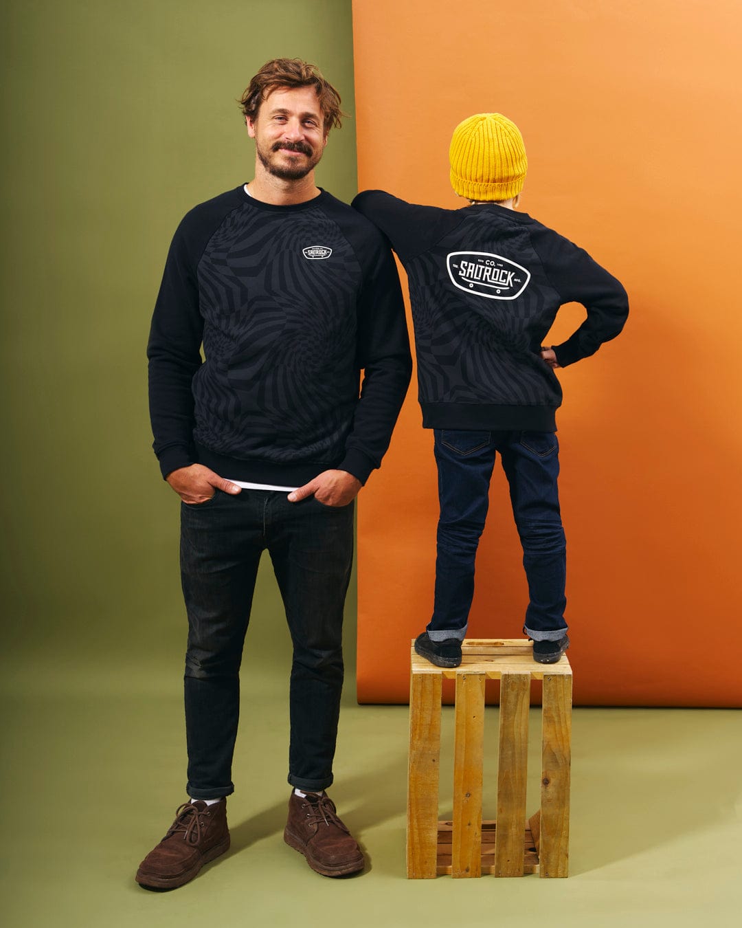 A man and child confidently posing next to each other in matching black sweatshirts featuring the captivating geometric print from Saltrock branding. Their hands firmly hold onto their skateboards displaying the Saltrock Grip It - Mens Crew Neck Sweat - Black.