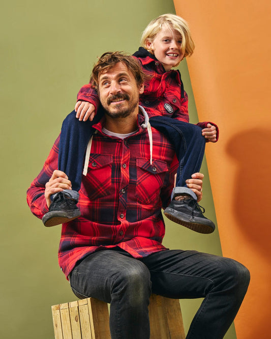 A man and child, both wearing the Saltrock Hawkins Hooded Long Sleeve Check Shirt in Red, sitting on top of a wooden box.