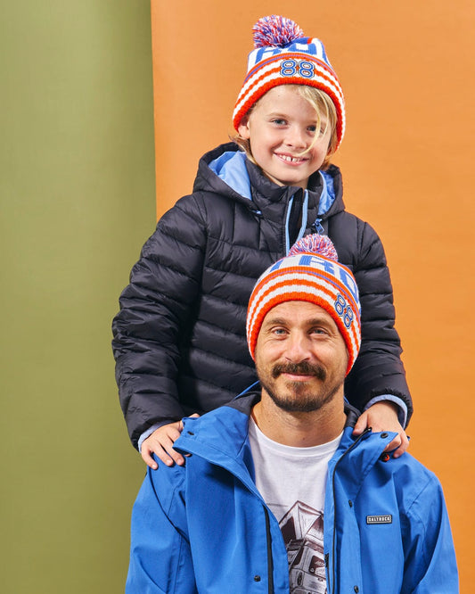 A man and a child, both wearing Saltrock Apres - Beanie - Blue beanies with pom poms, posing for a photo.