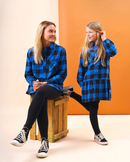 A mother and daughter in matching Saltrock Birdie - Girls Check Shirt Dresses - Blue, made from 100% cotton, featuring a smock silhouette and adorned with blue and black plaid flannel jackets.