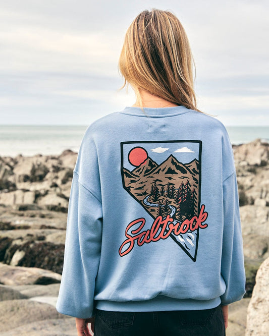 The back of a woman wearing a blue sweatshirt with a Saltrock Mountain Creek Almira - Womens Balloon Sleeve Sweat design perfect for everyday wear.