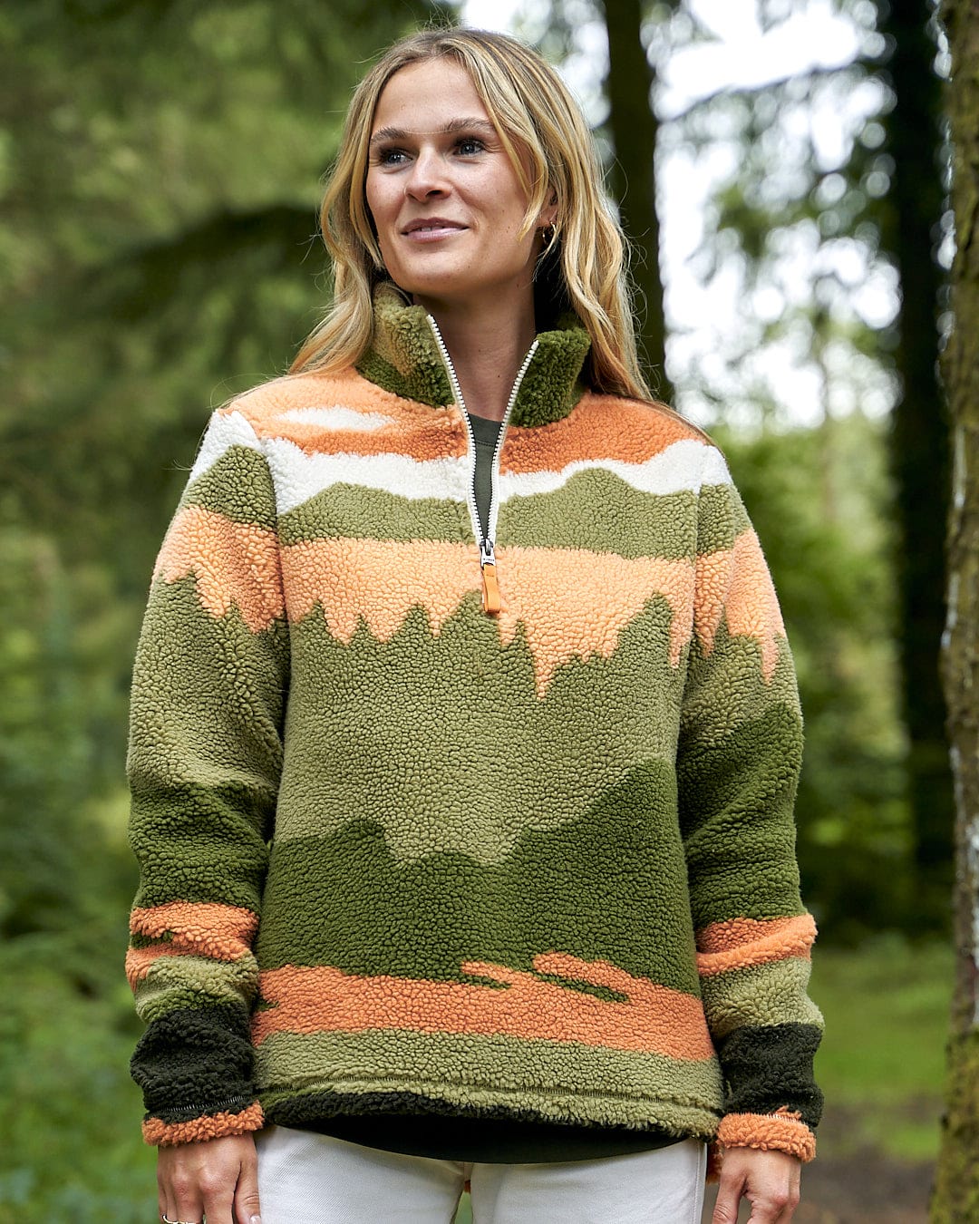 A woman is standing in the woods wearing a Saltrock Mountain Scape - Womens 1/4 Fleece - Orange sweater.