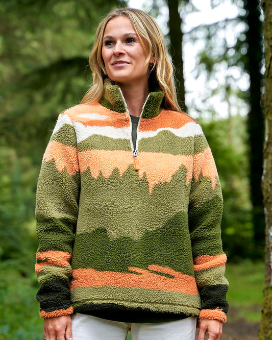A woman is standing in the woods wearing a Saltrock Mountain Scape - Womens 1/4 Fleece - Orange sweater.