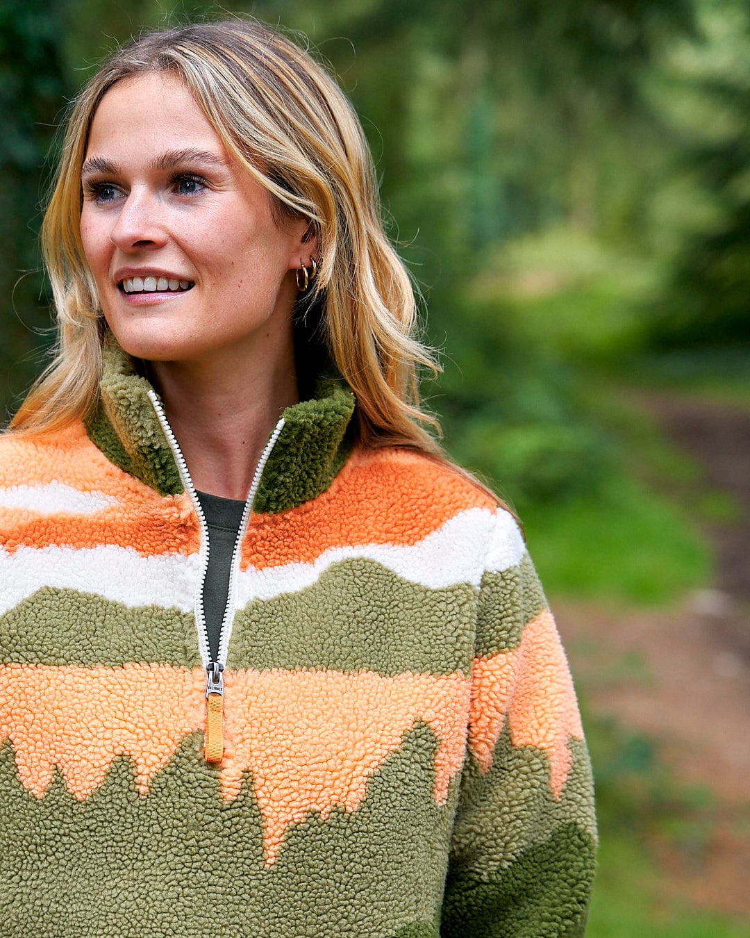 A woman in a Saltrock Mountain Scape - Womens 1/4 Fleece - Orange sweater standing in a wooded area.