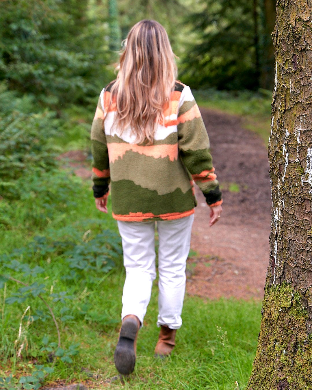 A woman walking through a wooded area wearing the Mountain Scape - Womens 1/4 Fleece - Orange by Saltrock.