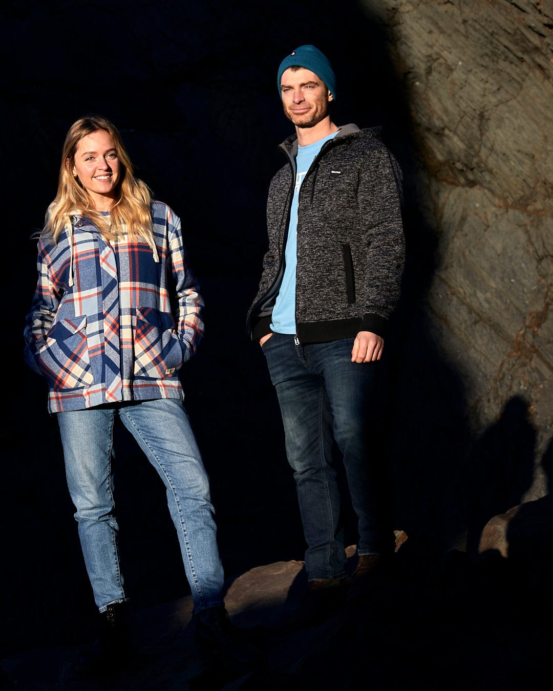 A man and woman standing in front of a rock with Saltrock's Myla - Womens Hooded Checked Shacket - Blue Check zips fastening on their front pockets.