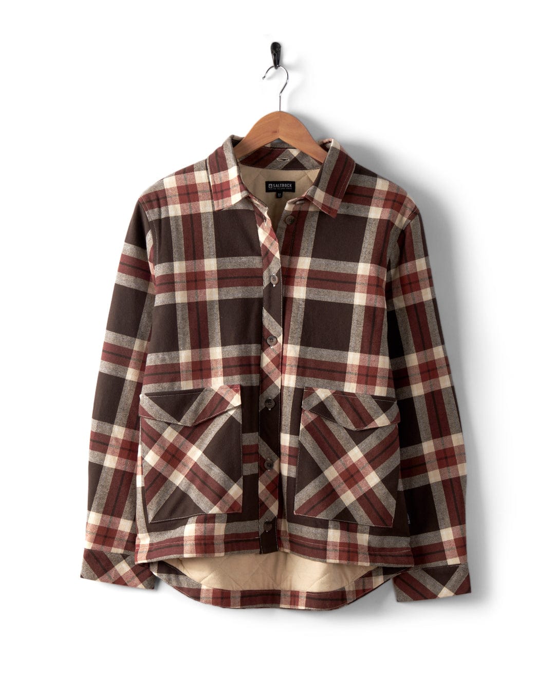 The Saltrock Myla Women's Hooded Shacket in brown features a check plaid design, oversized fit, button-up front, two large pockets, and is displayed on a wooden hanger against a white background.
