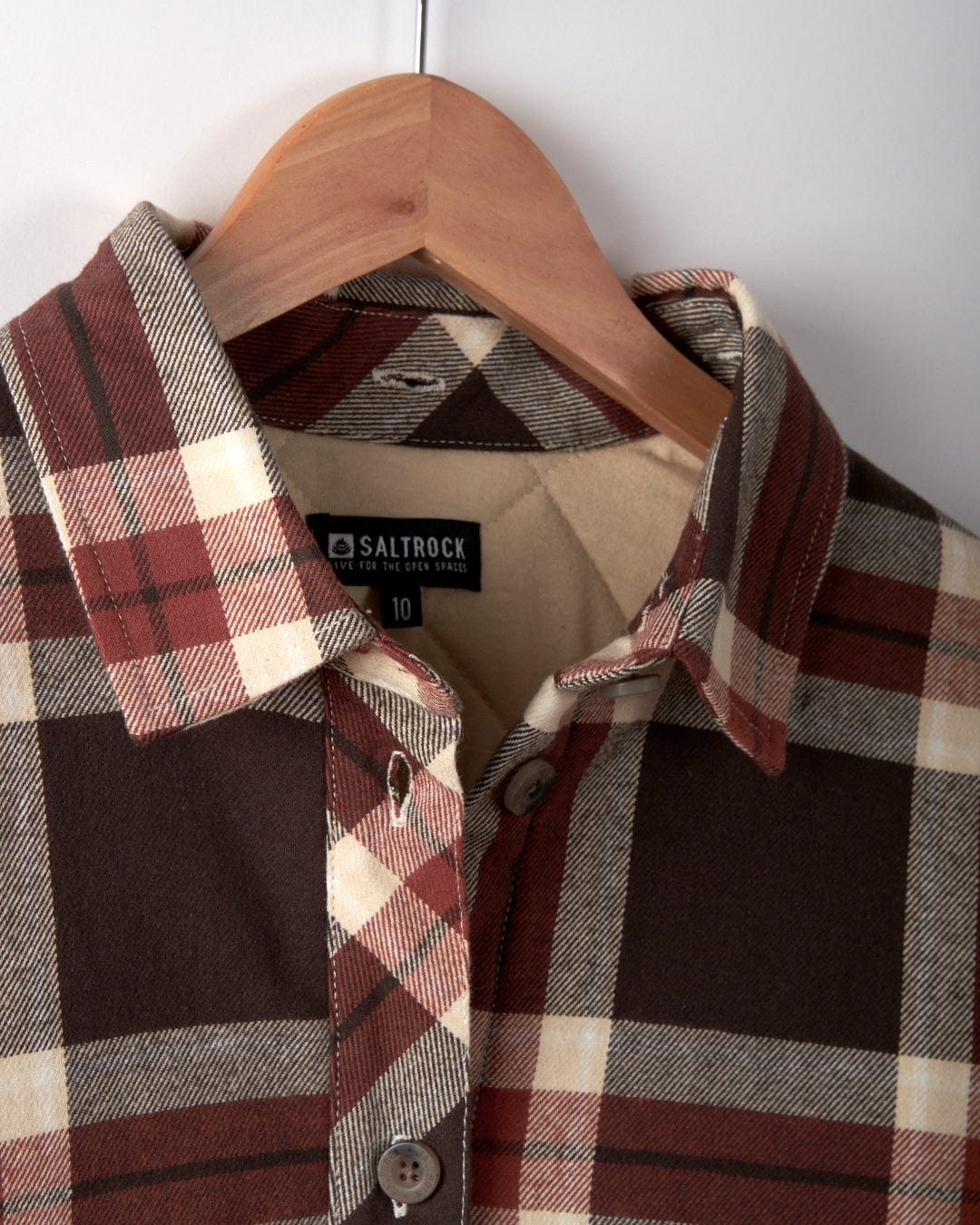 The Saltrock Myla Women's Hooded Shacket in brown check plaid, size 10, is displayed on a wooden hanger. It features an oversized fit for comfort and includes a visible Saltrock brand label.