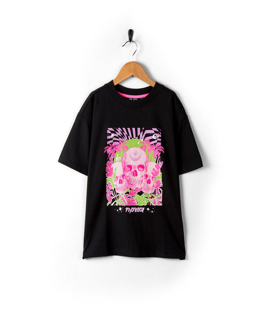 A Mystic Skulls - Recycled Kids Short Sleeve T-Shirt - Black by Saltrock with a bright pink and white skull illustration hanging on a hook against a white wall.