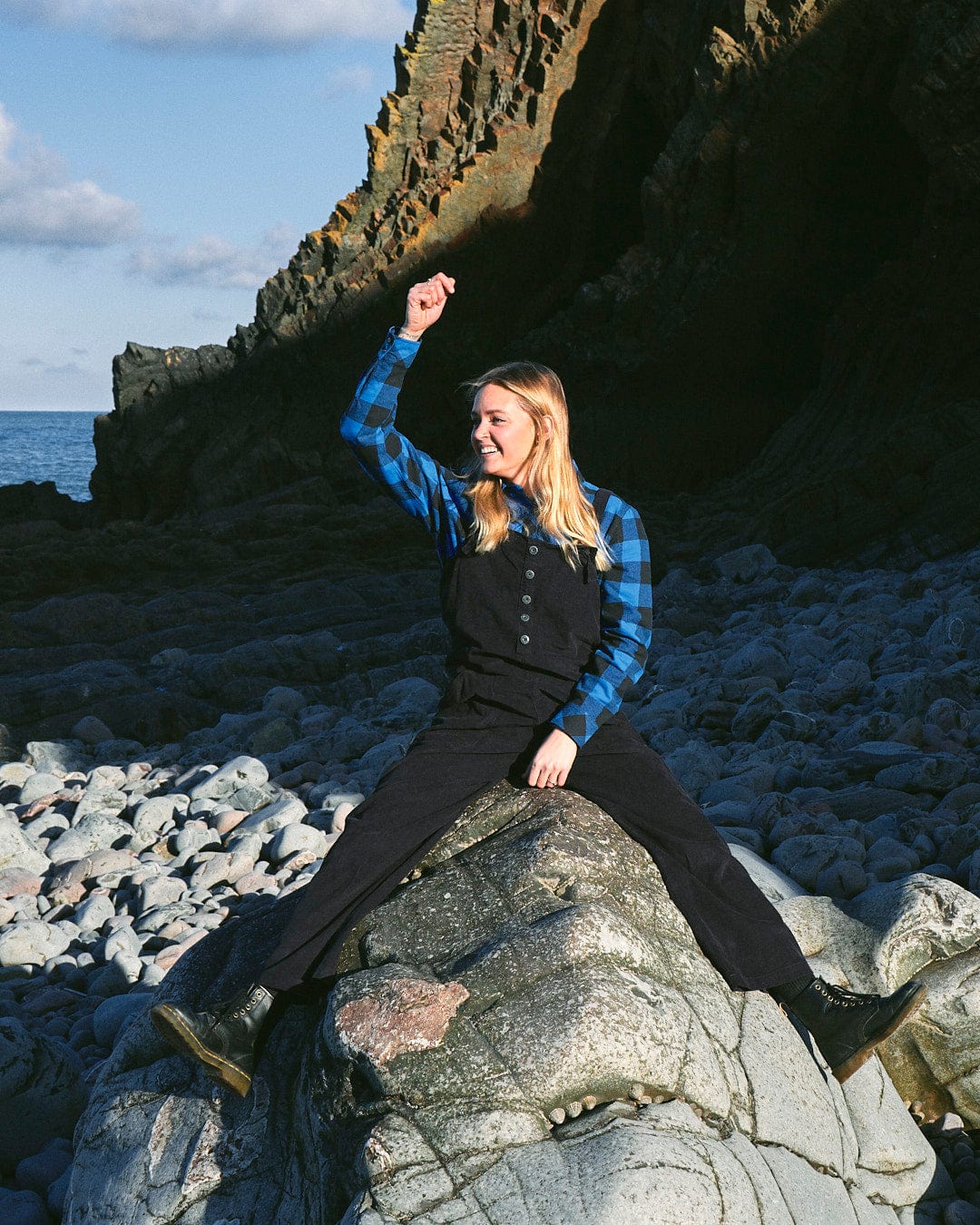 A fashion-conscious woman is sitting stylishly on top of a rock wearing Nancy - Womens Cord Dungaree in Dark Blue by Saltrock.