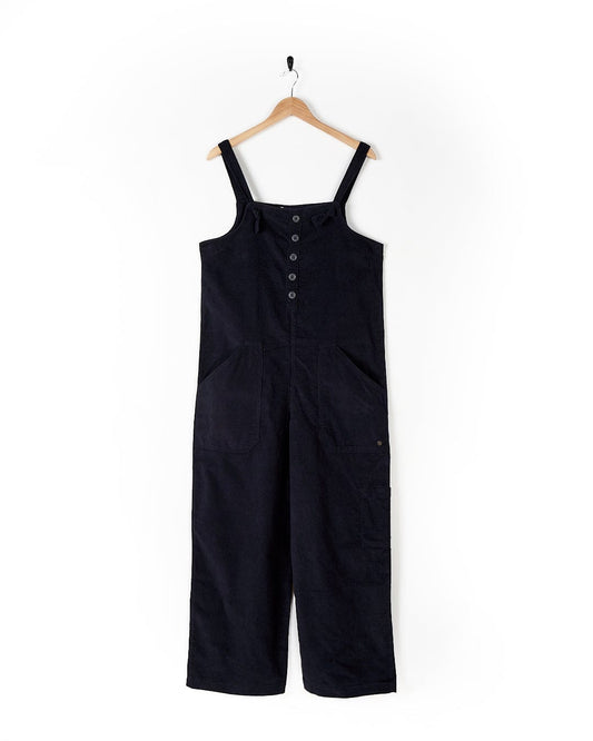 A Nancy - Womens Cord Dungaree - Dark Blue jumpsuit hanging on a hanger with the Saltrock brand.