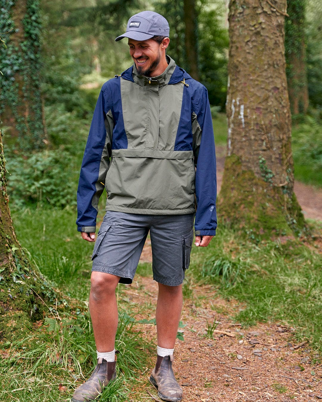 A man engaging in outdoor activity, standing in the woods, wearing a Saltrock Nevis - Mens Waterproof Mac - Blue/Green jacket.