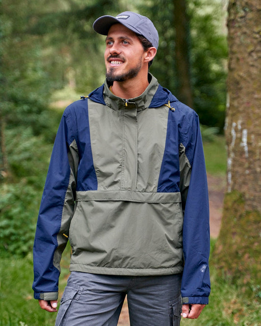 A man is walking through the woods with a Saltrock Nevis - Mens Waterproof Mac - Blue/Green jacket.