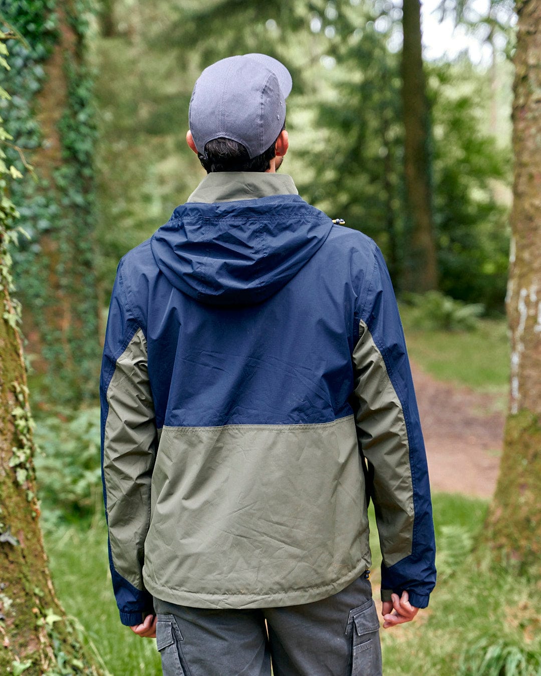 The back of a man wearing a Saltrock Nevis - Mens Waterproof Mac - Blue/Green in the woods.