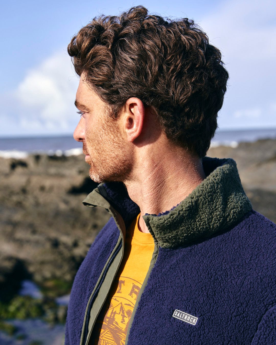 A man in a blue jacket, Odin - Mens Zip Thru Fleece by Saltrock, looking at the ocean.