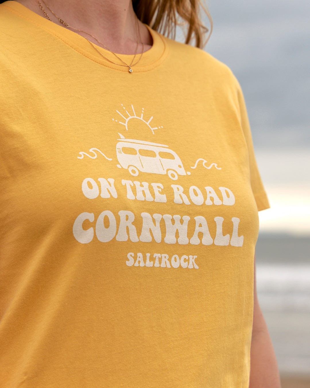 A woman wearing a yellow t-shirt that says On The Road Cornwall Saltrock.