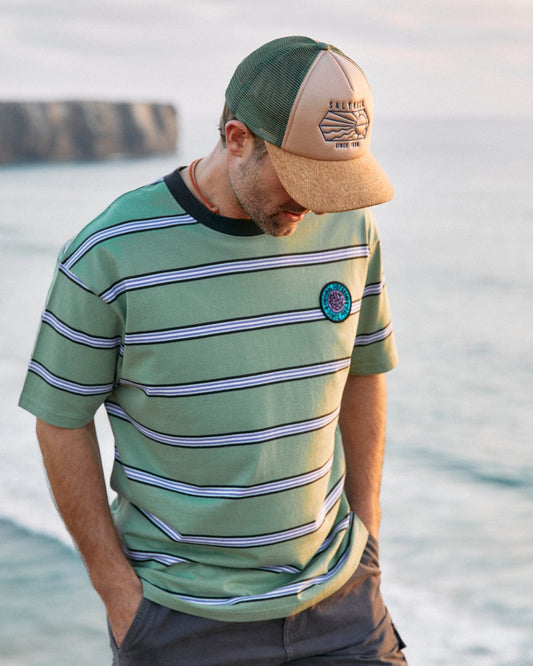 Man in a Saltrock Original Mens Short Sleeve T-Shirt in Green and cap standing by the sea at sunset.