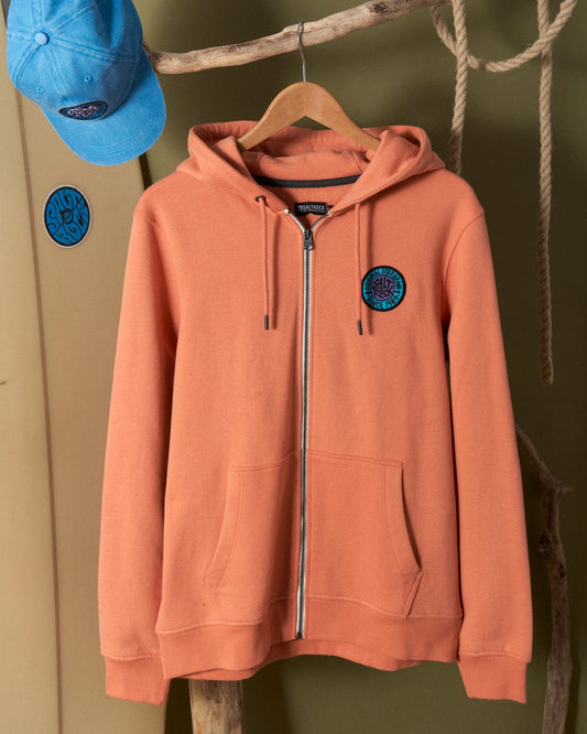Saltrock Orange hoodie with branded metal eyelets and badges hanging on a wooden peg beside a blue cap attached to a green wall.