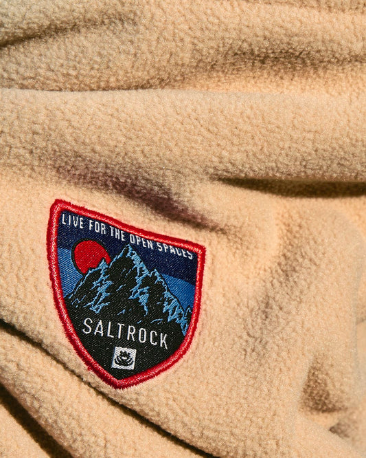 A close up of a Patchy - Borg Snood - Beige with a Saltrock mountain scene patch.