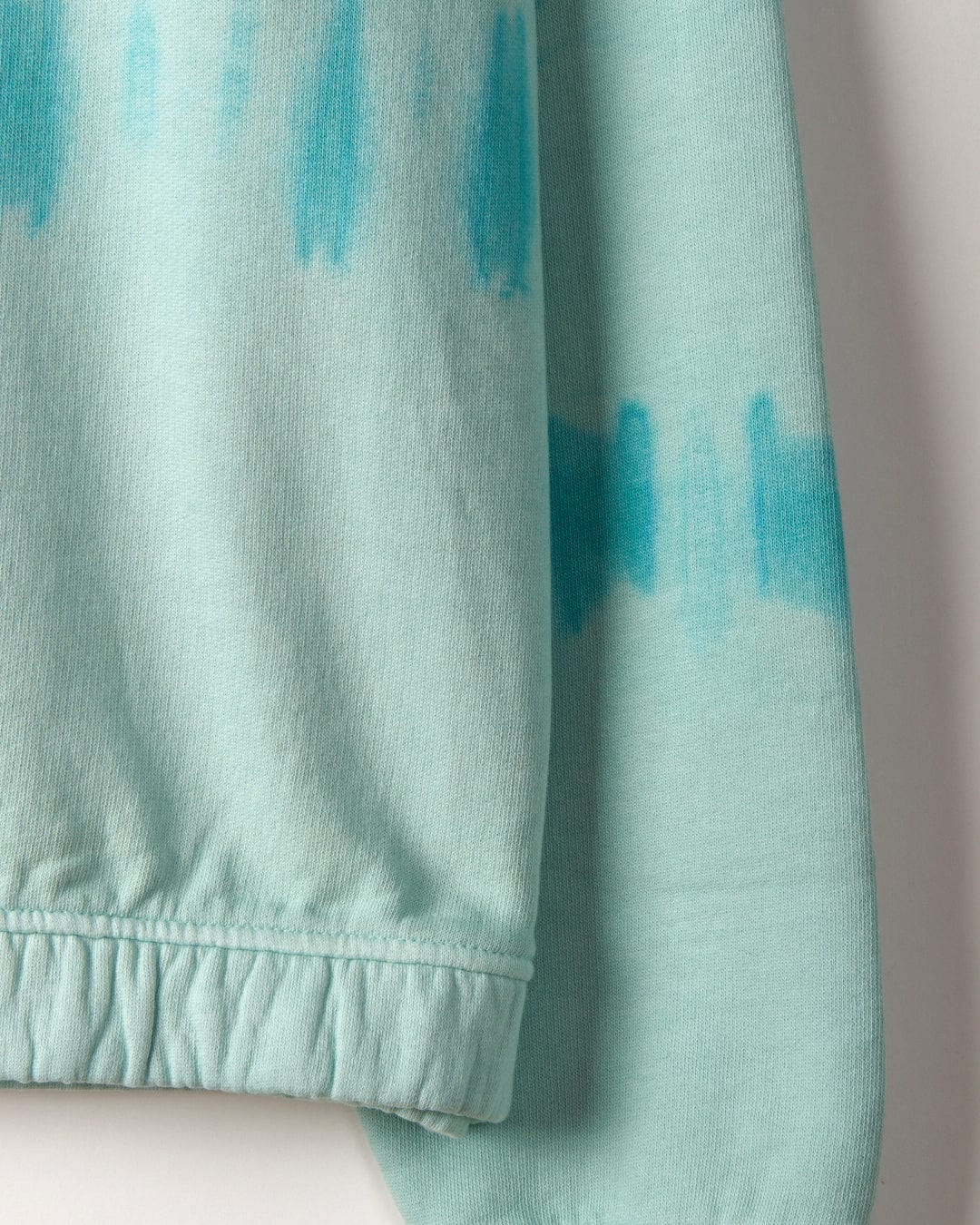 Close-up of a Peace Love - Kids Sweat - Green fabric by Saltrock with darker turquoise tie dye stripe and a detailed view of the fabric's texture and stitched hem.