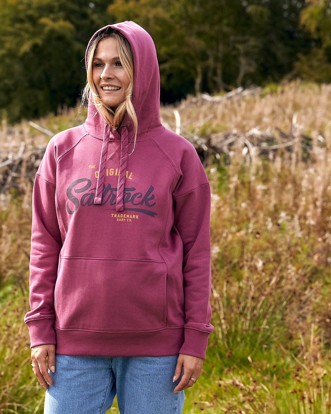 A woman is standing in a field wearing a Saltrock Pennie - Ladies Pop Hoodie - Dark Pink.