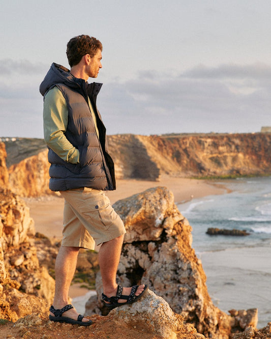 Man standing on a rock, wearing Saltrock's Penwith II - Mens Cargo Shorts in Cream, gazing at the seaside view during sunset.