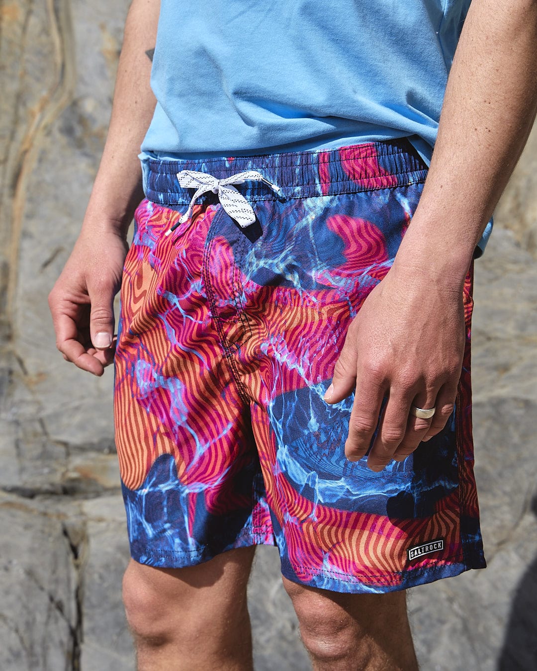 A man wearing a Saltrock Poolside - Mens All Over Print Swimshort - Teal t-shirt and blue shorts.