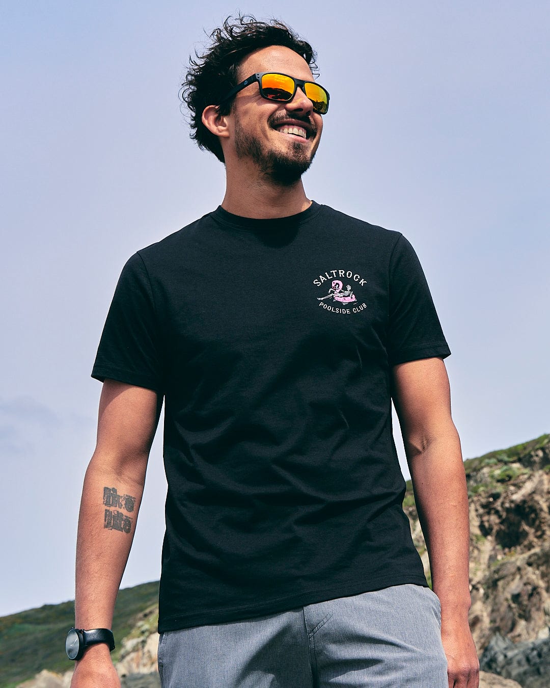 A man wearing sunglasses and a Poolside Club - Mens Short Sleeve T-Shirt - Black by Saltrock.