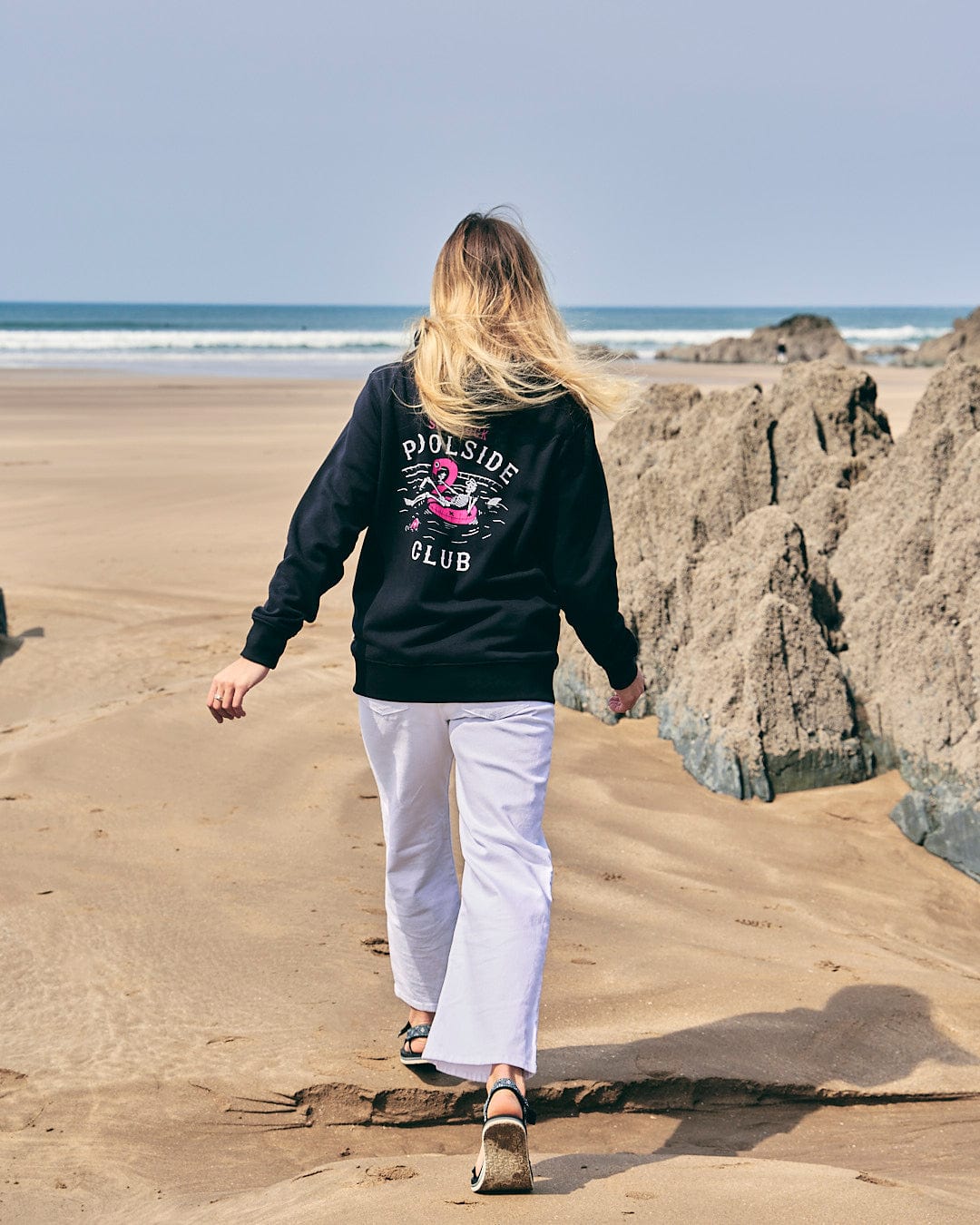 A woman walking on the beach wearing a Saltrock Lee-Ann - Womens Zip Hoodie - Black.