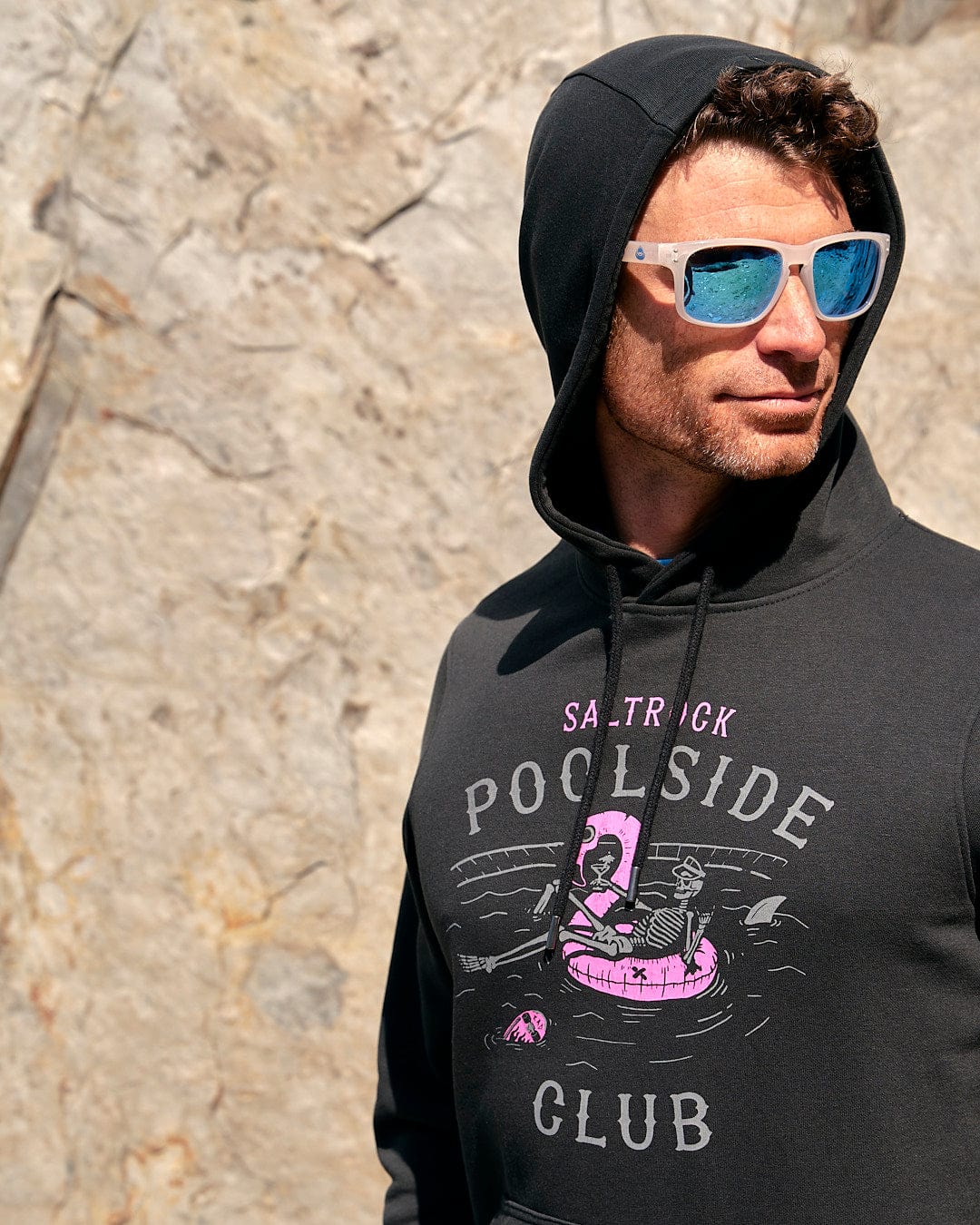 A man wearing a Saltrock hoodie with the words "Poolside - Mens Pop Hoodie - Black" on it.