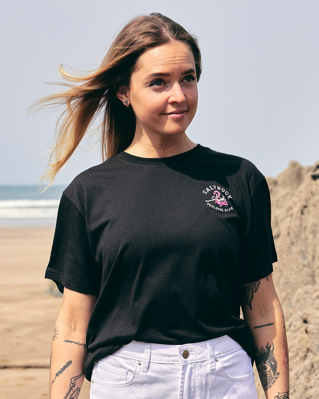 A woman wearing a Saltrock Poolside - Womens Short Sleeve T-Shirt - Black standing on the beach.