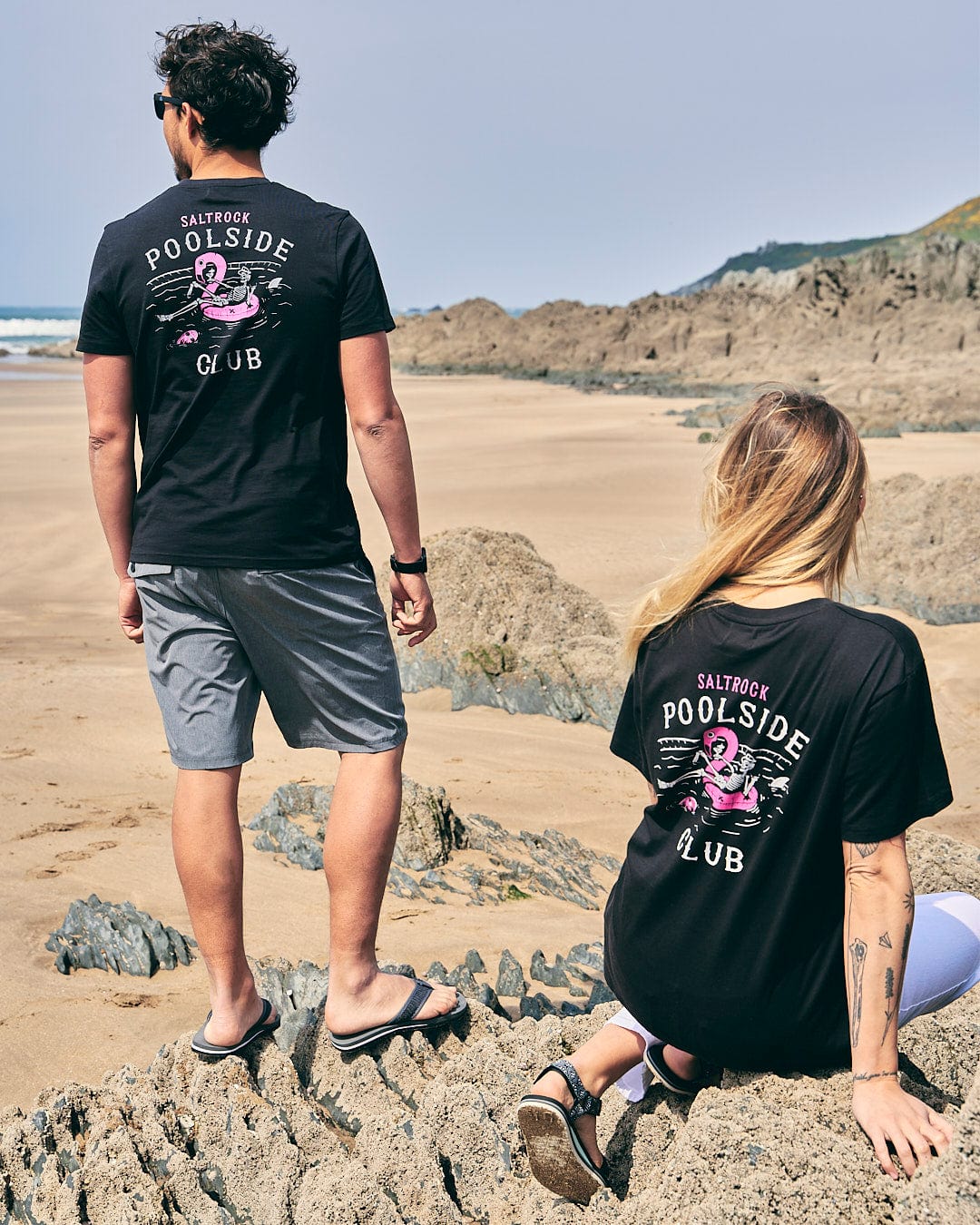 A man and woman standing on rocks at the beach wearing Saltrock's Poolside - Womens Short Sleeve T-Shirt - Black.