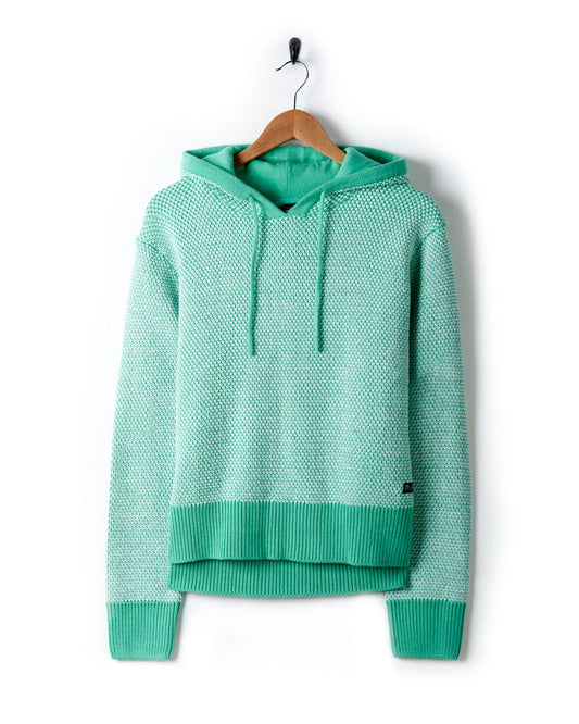 A Saltrock Poppy - Womens Knitted Pop Hoodie - Green with a textured knit and lined hood is hanging on a wooden hanger against a white background.