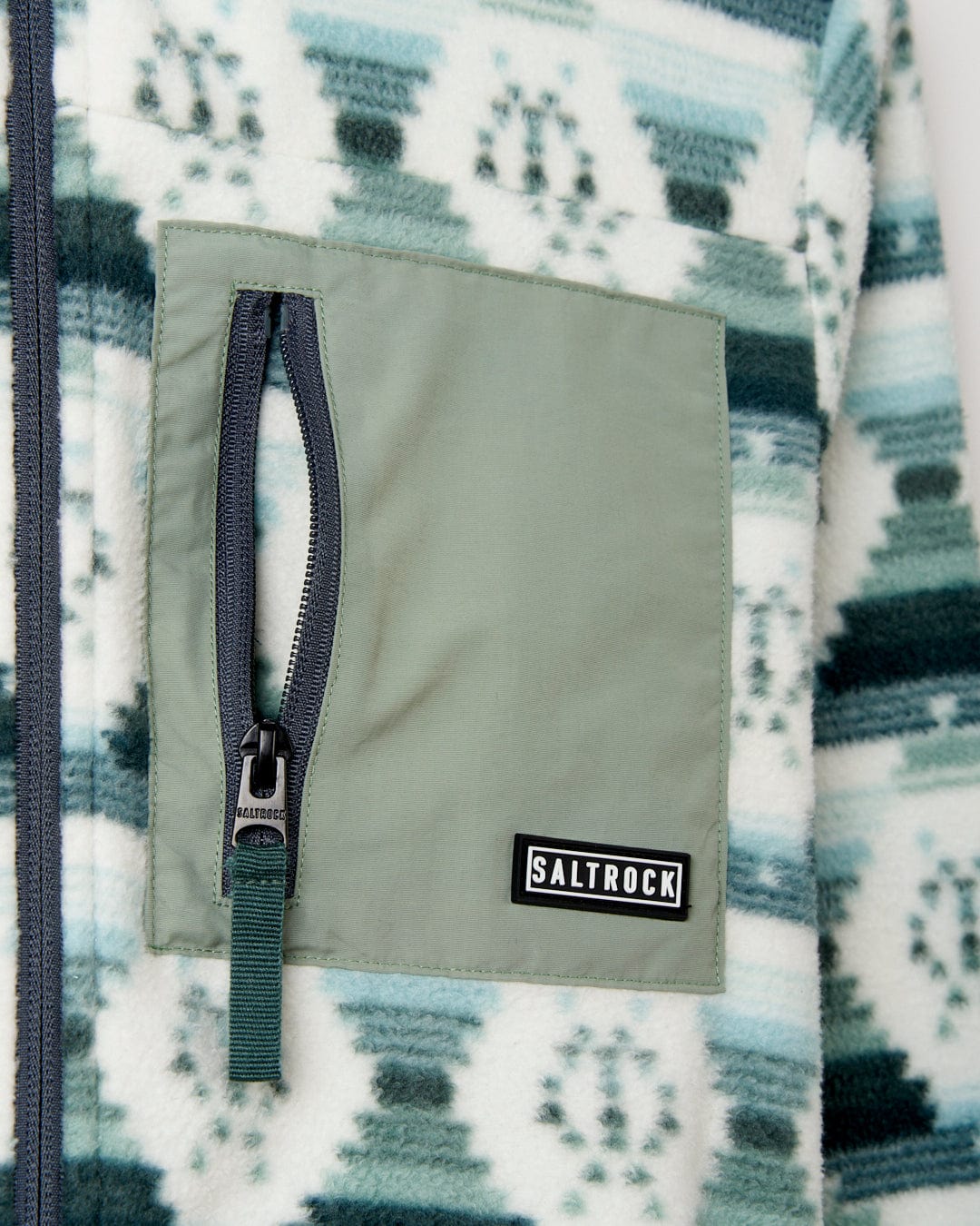 A close-up of a green zipper pocket on a Portis Women's Fleece in green with a blue and green Aztec print, featuring a Saltrock brand tag.