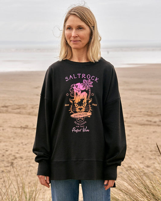 A woman wearing a Saltrock Purfect Wave Gradient - Womens Boyfriend Fit Sweat - Black standing on the beach.
