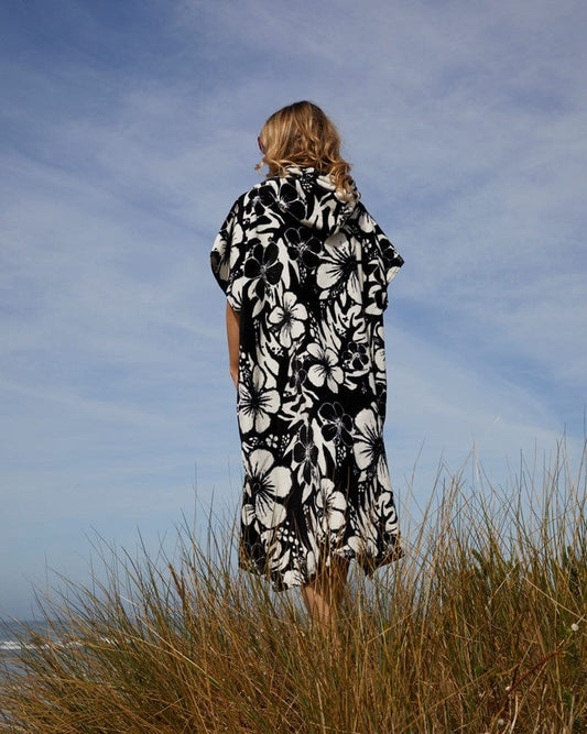 A person in a Saltrock 100% cotton black and white Hibiscus changing towel stands facing the horizon in a field of tall grass under a clear blue sky.